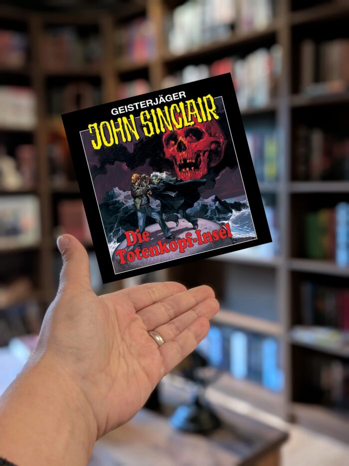 Jason Dark: Geisterjäger John Sinclair - Die Totenkopf-Insel: Schwarzes Cover mit weißer und gelber Schrift. Man sieht auf einem Felsen zwei Männer kämpfen, im Hintergrund sieht man Wasser und einen roten Totenkopf.