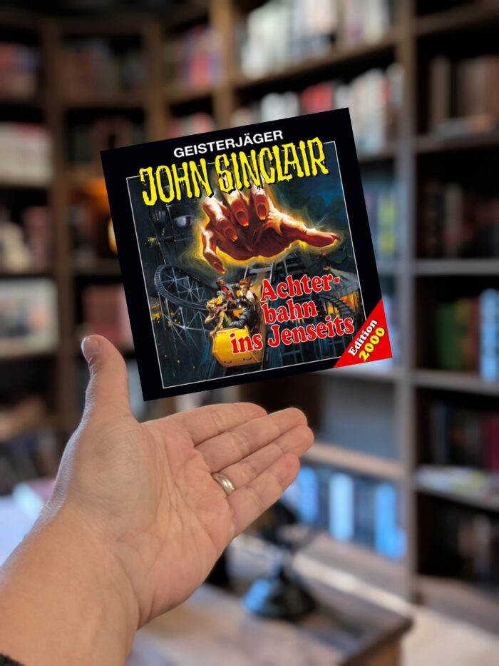 Jason Dark: Geisterjäger John Sinclair - Achterbahn ins Jenseits: Schwarzes Cover mit roter und gelber Schrift, man sieht verschreckte Menschen in einer Achterbahn und darüber schwebt eine große, glühende Hand.